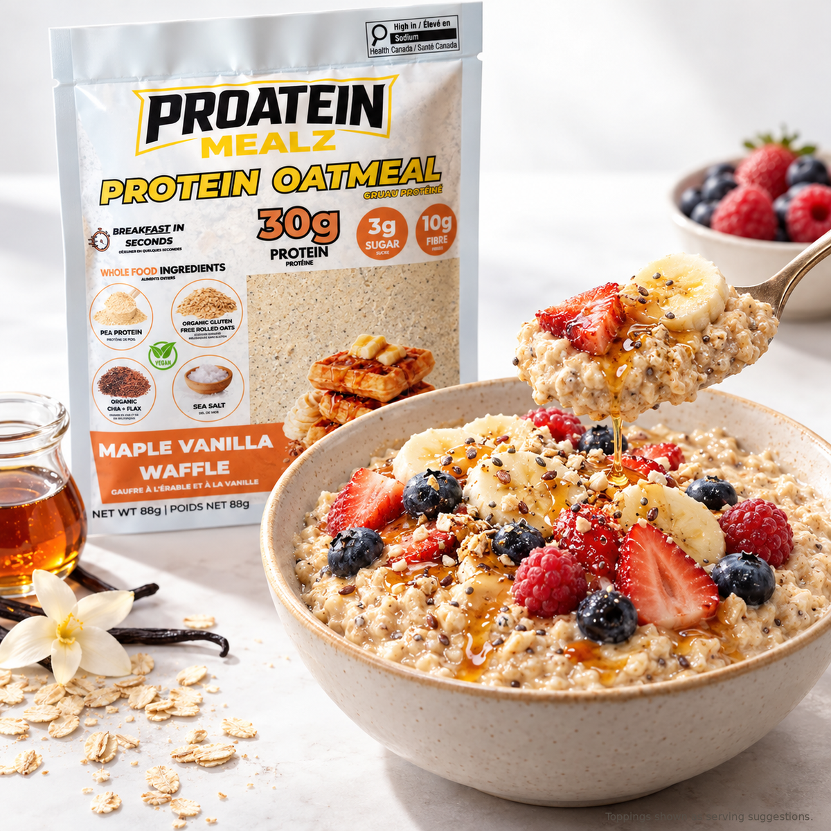 A bowl of protein oatmeal topped with strawberries, blueberries, banana slices, and honey, with a spoon lifting the oatmeal. A stand-up pouch of Proatein Mealz Protein Oatmeal Maple Vanilla Waffle is visible behind the bowl, along with oats, a flower, vanilla bean, and a small jar of honey on a light marble surface.